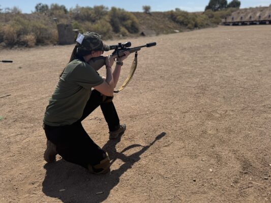 Woman shooting rifle in kneeling position.